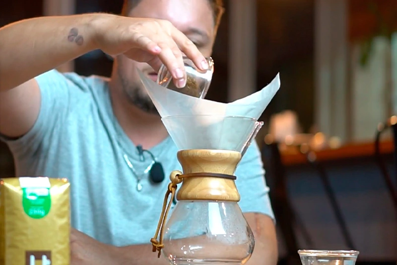 Barista acrescentando café moído na hora para preparo de café coado