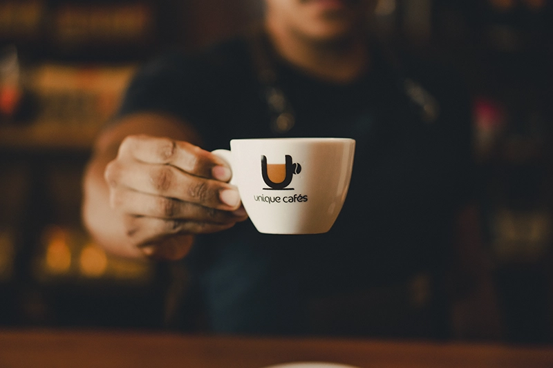 Barista segurando uma xícara de café especial de frente para câmera.